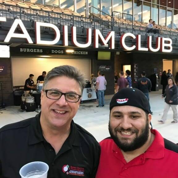 Two men are smiling and posing for a photo outside a venue marked 